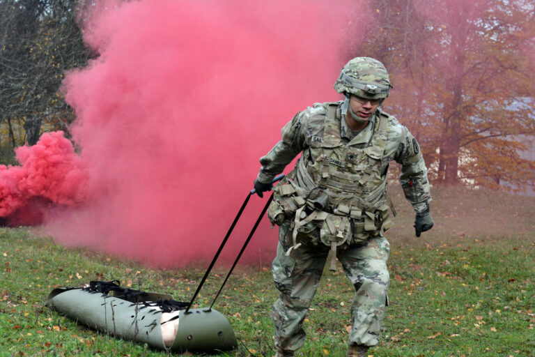 A man in camp pulls a SKED away from bright red smoke